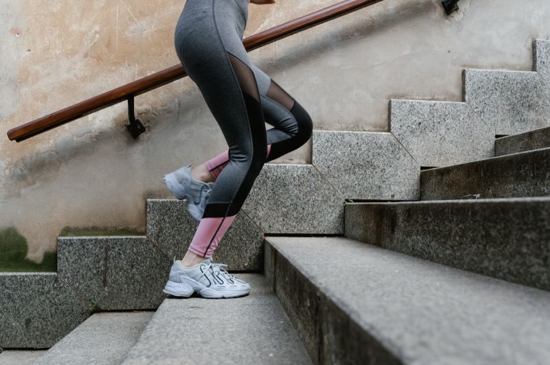 część sylwetki ludzkiej w sportowym stroju biegnąca po schodach